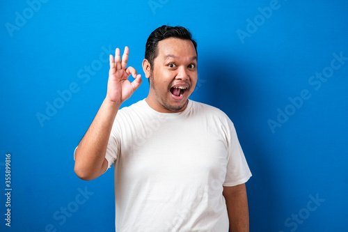 Young Fat Asian man smiling with ok sign. Happy asian man over blue background doing okay sign.