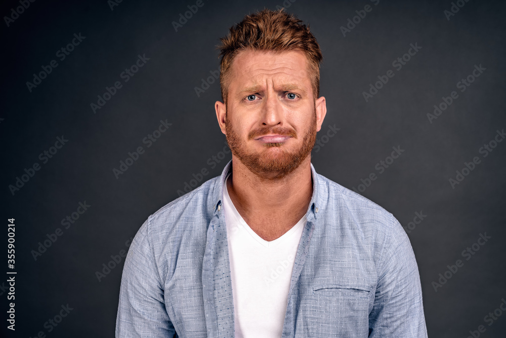 Horizontal shot of attractive red male model with unhappy expression curves lips as feels frustration, being upset to hear bad news, isolated over white background. Negative human facial expressions Horizontal shot of attractive red male model with unhappy expression curves lips as feels frustration, being upset to hear bad news, isolated over white background. Negative human facial expressions