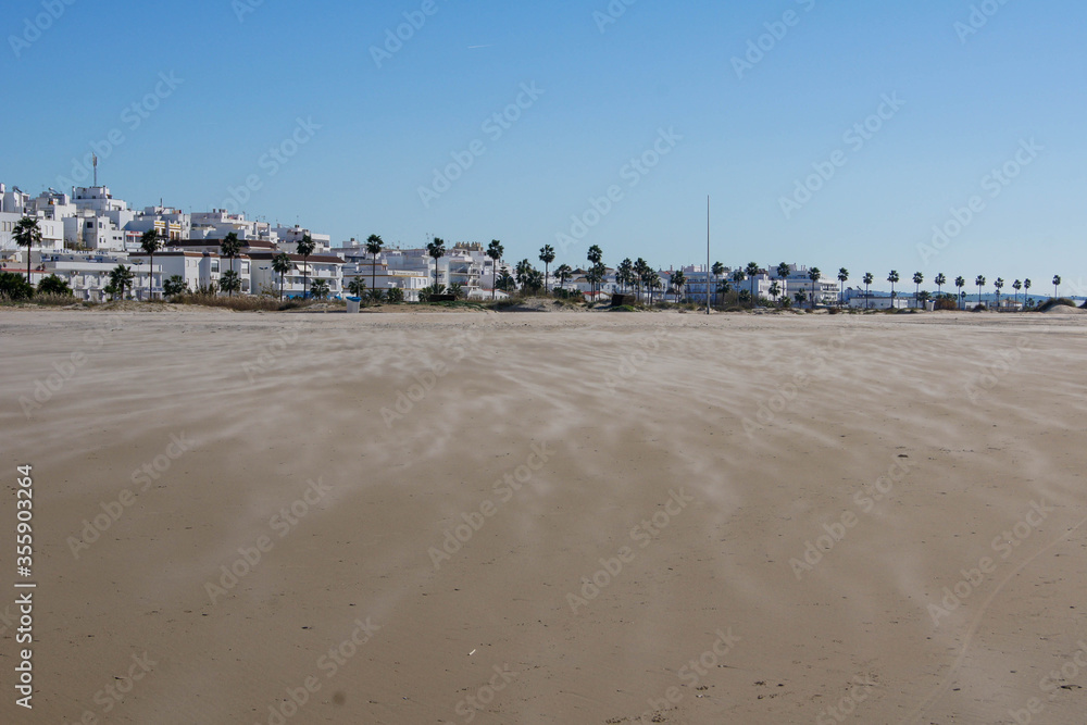 Conil de la Frontera / Spain - December 31, 2016 - Panoramic view from the beach side of the village of Conil at Costa de la Luz, Spain (Andalucia) under a blue sky. Light sandstorm at the beach.