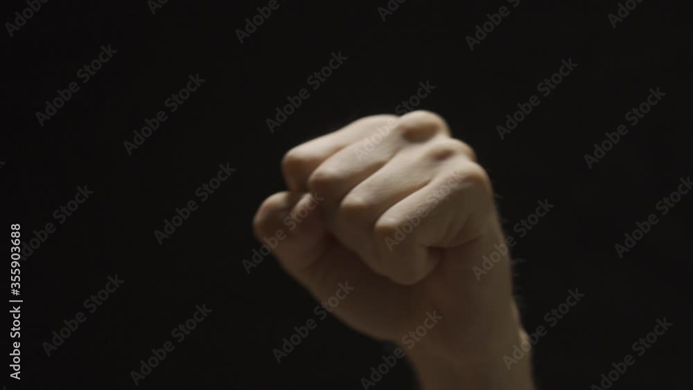 Hand doing a fist enters frame with black background - clenched and strong Hand doing a fist enters frame with black background - clenched and strong