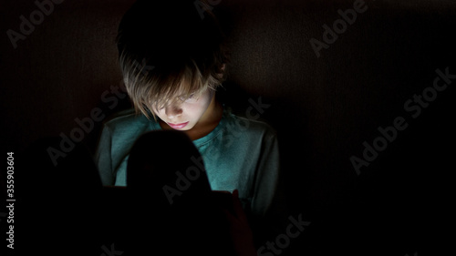 Young boy using smartphones sittingon a sofa at home, entertaining online obsessed with modern devices, gadget addiction