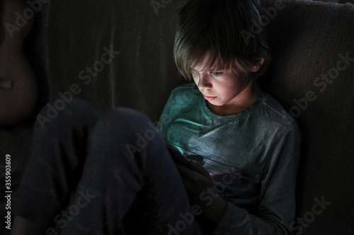 Fotografija Young boy using smartphones sittingon a sofa at home, entertaining online obsess