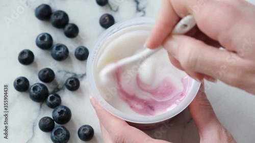Blueberry greek yogurt in jar. Person stirring blueberry filling with natural greek yogurt in plastic jar. Store bought blueberry yogurt