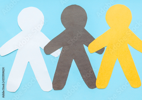 Flat lay  black, yellow, white paper people holding hands on blue background, top view. Unity concept. Stop racism, black lives matter, social exclusion message, misunderstanding, denial of society.