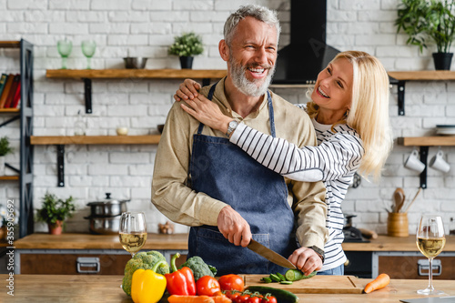 Senior couple spending time together while cutting vegetables at kitchen