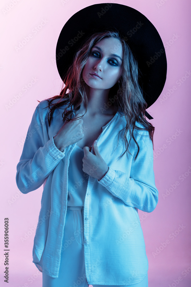 Closeup portrait of smiling teenager girl posing against pink neon wall, woman wearing white costume and black hat. People concept Closeup portrait of smiling teenager girl posing against pink neon wall, woman wearing white costume and black hat. People concept