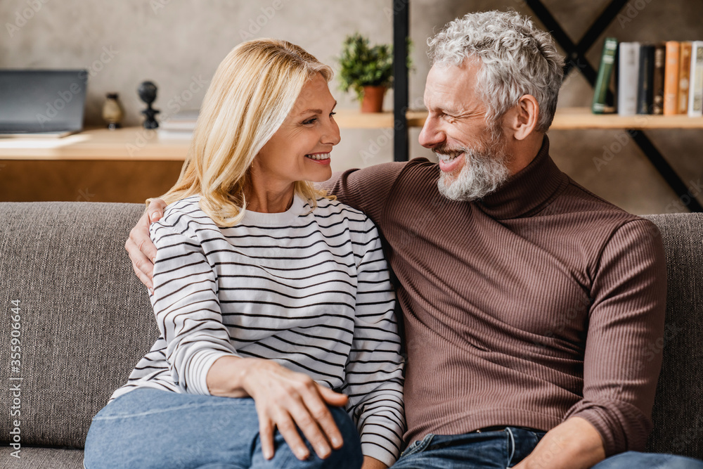 Middle aged couple relaxing and hugging on sofa at home with look on each other Middle aged couple relaxing and hugging on sofa at home with look on each other