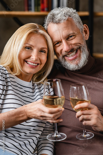 Vertical shot of cheerful middle aged couple enjoying wine at home