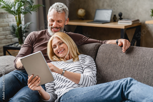 Happy senior couple using digital tablet on sofa indoors photo