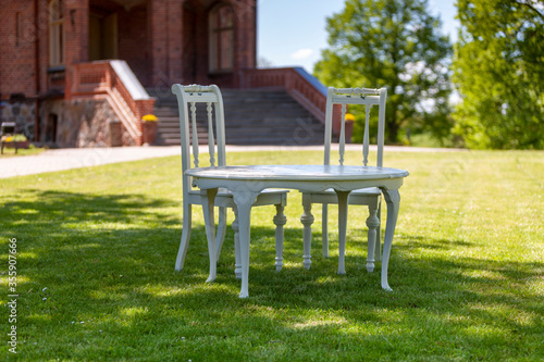 Outdoor white table and chairs on a green lawn near a brick building with a wide staircase. © Eleonora