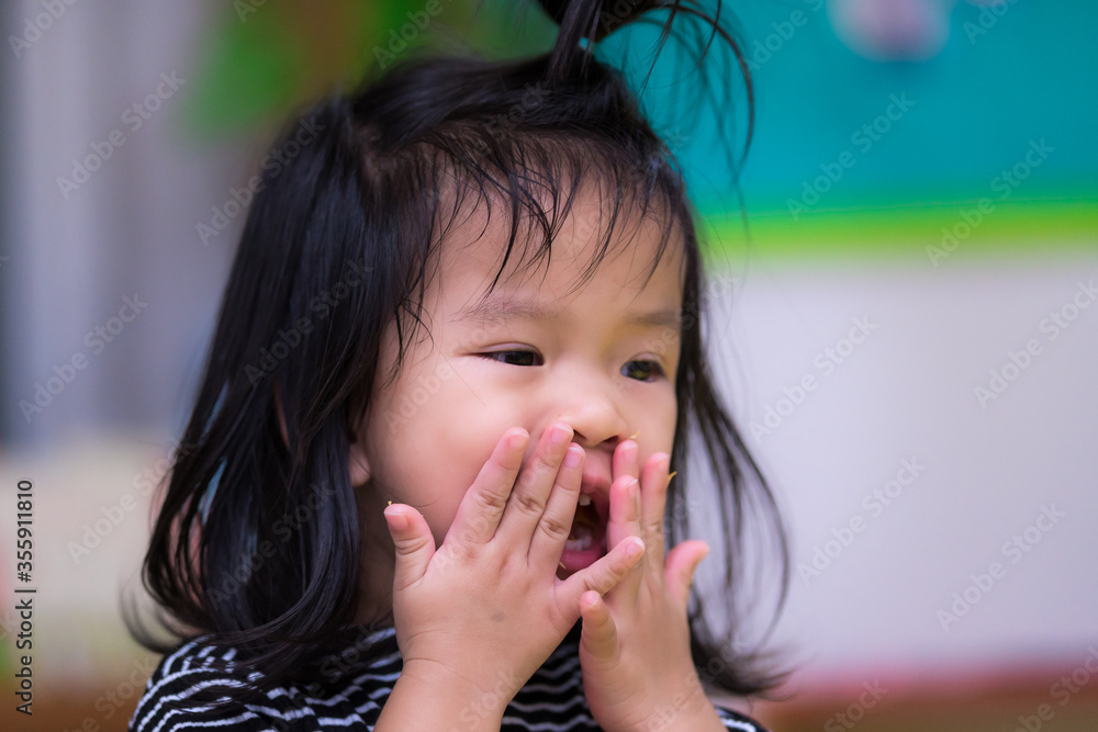 Portrait of one child little girl flick the candy crumb that is stuck on her face. The girl eats sloppy snacks on her hands and mouth. A cute Asian kid girl is 3 years old. Portrait of one child little girl flick the candy crumb that is stuck on her face. The girl eats sloppy snacks on her hands and mouth. A cute Asian kid girl is 3 years old.