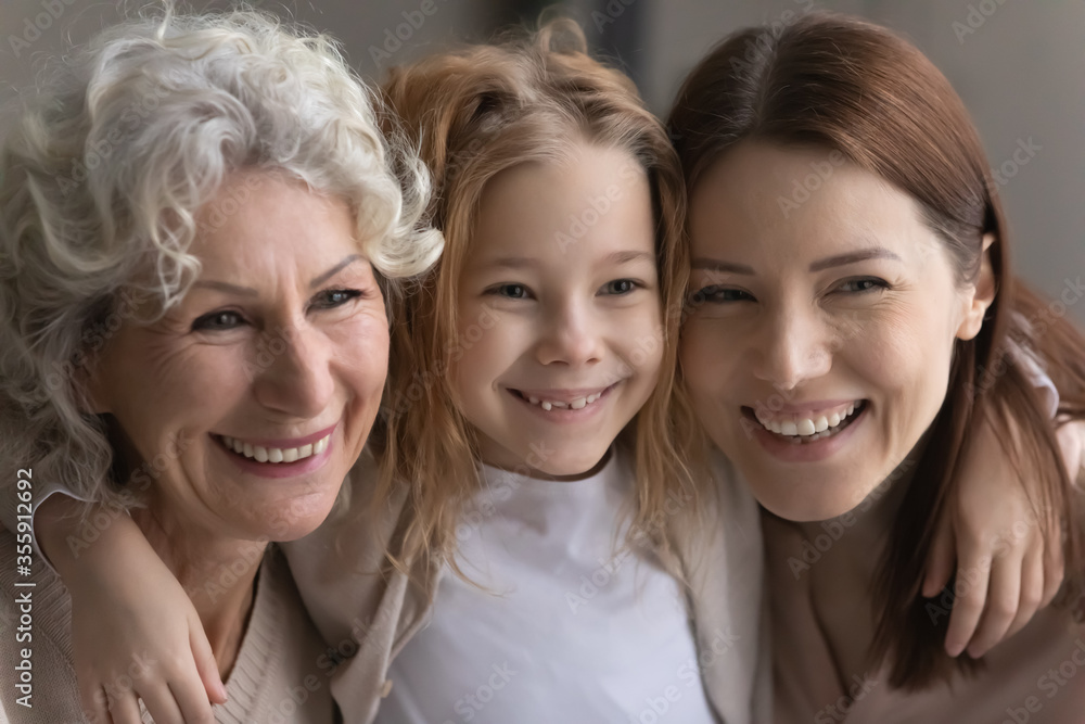 Close up portrait of happy three generations of women hug and cuddle show family unity and support, caring little girl with young mother and mature grandmother embrace, show love and bonding Close up portrait of happy three generations of women hug and cuddle show family unity and support, caring little girl with young mother and mature grandmother embrace, show love and bonding