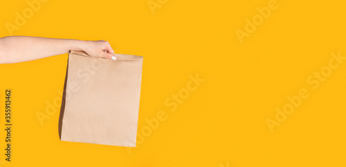 Принти на полотні Millennial woman holding paper bag with takeaway food on orange background, empt