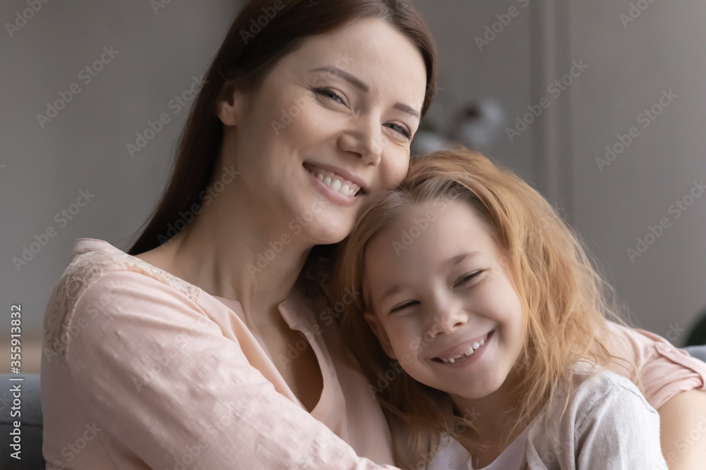 Close up portrait of smiling young Caucasian mother and small daughter hugging and cuddling at home, show love and care, happy mom or nanny have fun play embrace cute little preschooler girl child Close up portrait of smiling young Caucasian mother and small daughter hugging and cuddling at home, show love and care, happy mom or nanny have fun play embrace cute little preschooler girl child