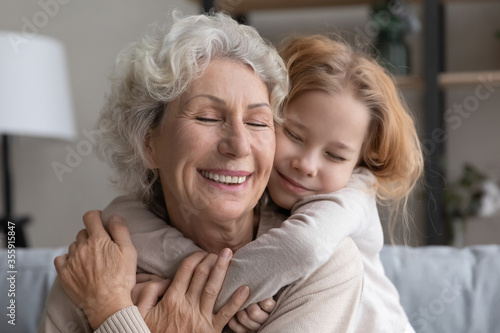 Cute caring small granddaughter embrace cuddle smiling middle-aged 60s grandmother, relax together at home, little grandchild hug senior grandparent, show love and gratitude, family unity concept © fizkes