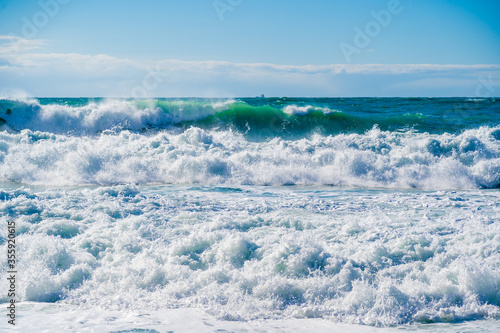 Green waves in white foam and spray rush through the stormy Black sea. The sun shines beautifully on the waves. Dangerous and beautiful. Blue-green gamma