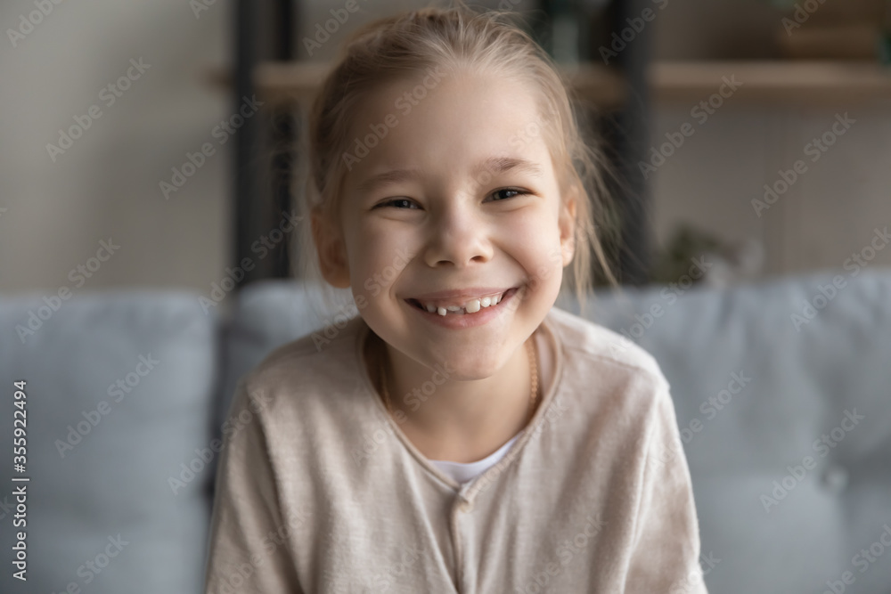 Close up headshot portrait of cute happy small preschooler girl with toothy smile look at camera posing, funny little child sit relax have fun on sofa in living room, feel optimistic and positive Close up headshot portrait of cute happy small preschooler girl with toothy smile look at camera posing, funny little child sit relax have fun on sofa in living room, feel optimistic and positive