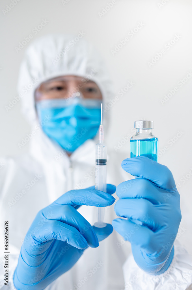 COVID-19 Vaccination concept. Doctor or physician in Personal protective equipment suit (PPE) with mask, goggles and rubber gloves holding syringe and medicine vial for Coronavirus vaccine injection. COVID-19 Vaccination concept. Doctor or physician in Personal protective equipment suit (PPE) with mask, goggles and rubber gloves holding syringe and medicine vial for Coronavirus vaccine injection.