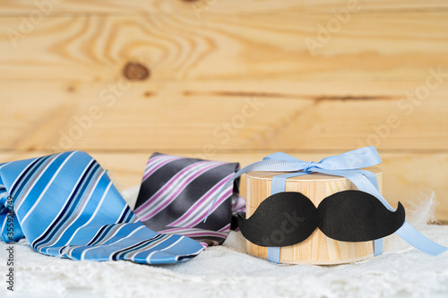 Happy Father Day background concept with gift box, black mustache and blue and pink necktie on wooden background with copy space for text.