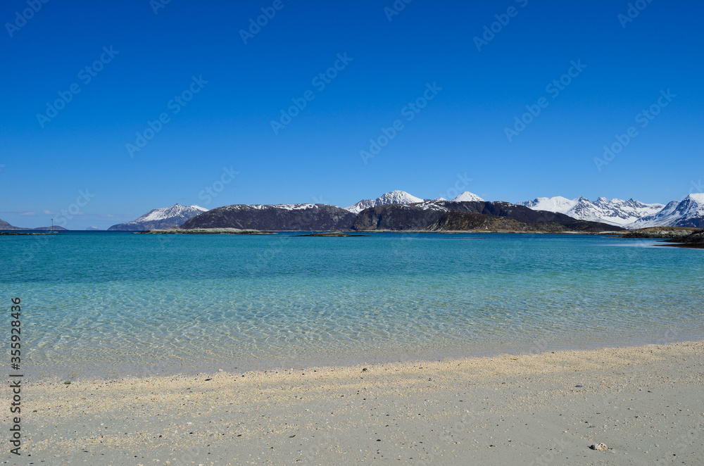 majestic white springtime beach with snowy mountain islands in sea on the summer island in northern norway