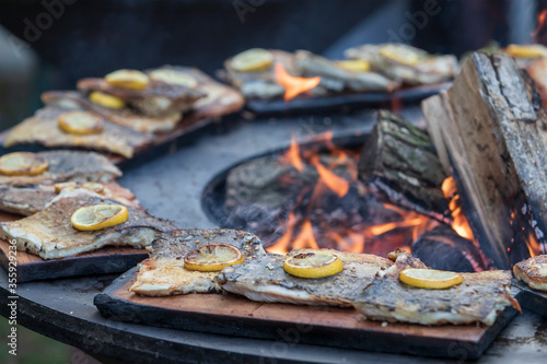 Fresh fish on the grill. A lemon wheel is placed on the fish. Fire can be seen in the middle.