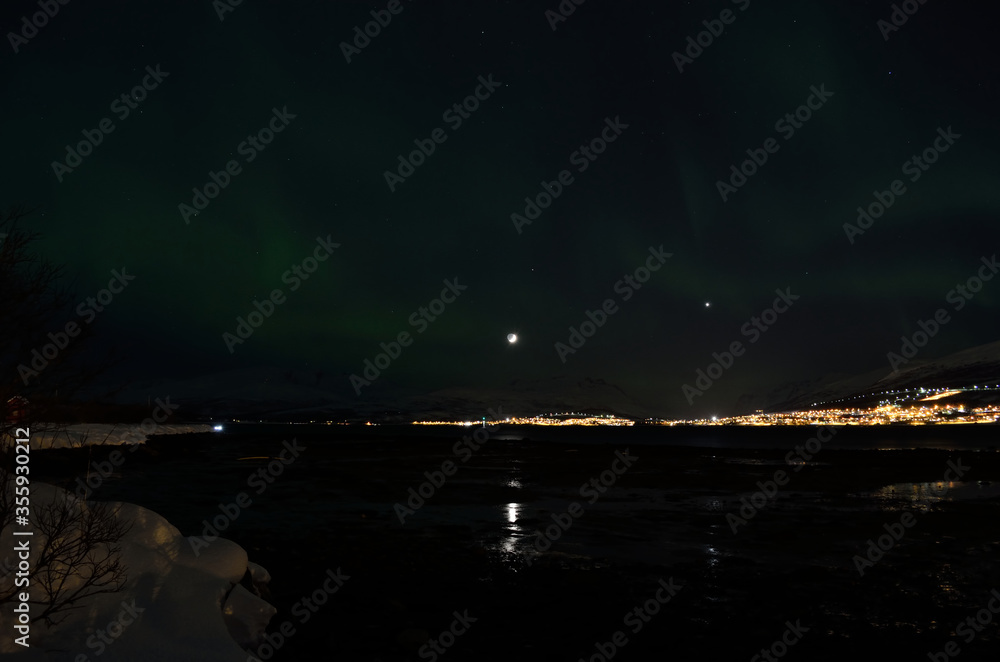 aurora borealis dancing over snowy mountain and fjord landscape with full moon light