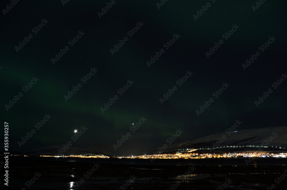 aurora borealis dancing over snowy mountain and fjord landscape with full moon light