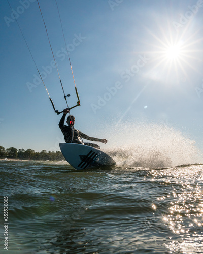 Portrait shot of wave kitesurfer doing a turn in the water while being backlit by a beautiful sun star
