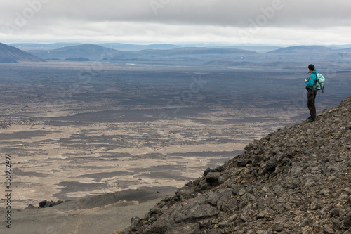 A park ranger stands on a hillside looking over Ódáðahraun in central Iceland. Volcanic landscape and mountains in the distance.