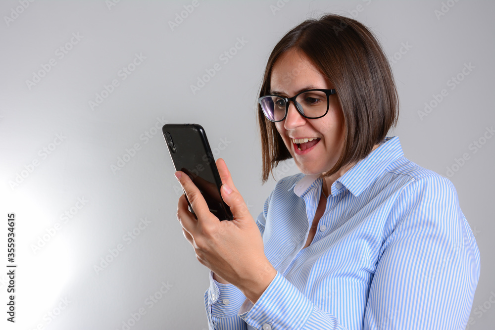 Excited beautiful woman receiving SMS in mobile phone over grey background.
