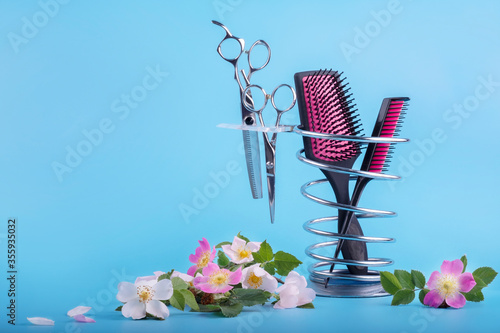 Hairdressing tools on a metal stand decorated with delicate pink flowers on a blue background. photo