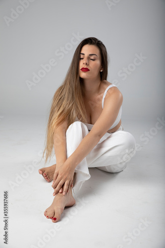 Modelo joven sentada sobre fondo blanco y ropa blanca con pelo largo