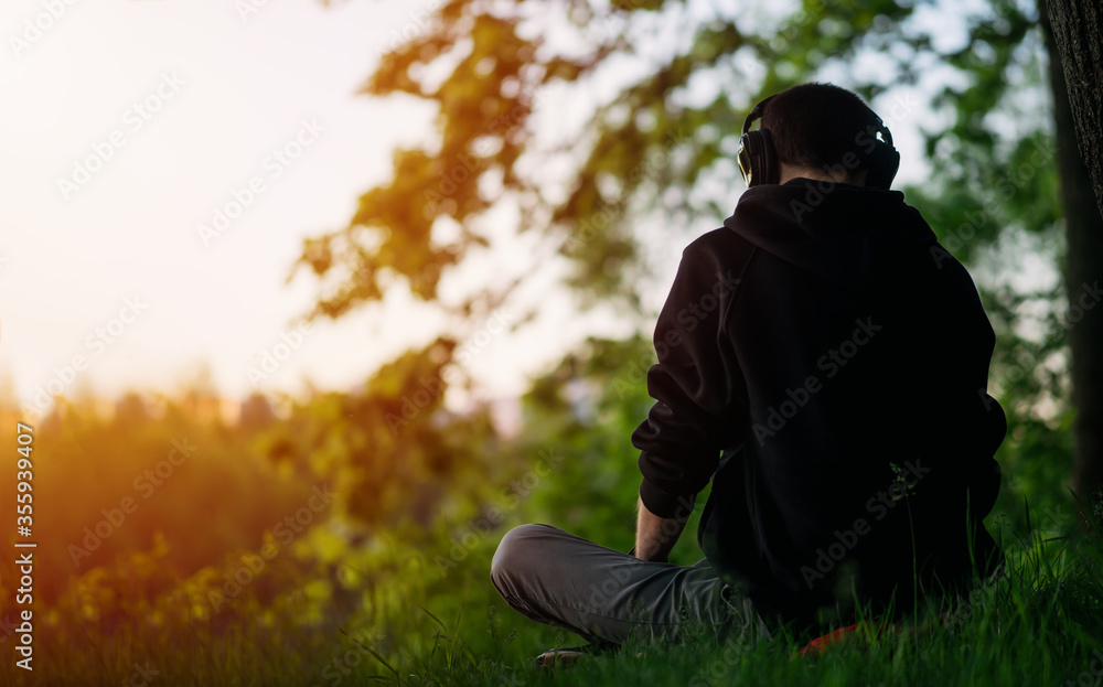 A man is sitting on the grass in a Park, listening to music and enjoying life. Back view A man is sitting on the grass in a Park, listening to music and enjoying life. Back view