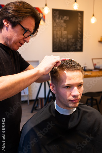 Barber is hairdressing the hair of young man with comb