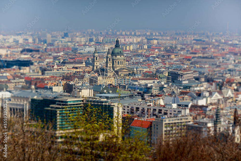 Obraz premium Beautiful morning top view of Budapest. Cathedral of St. Stephen and the Ferris wheel. Roofs of houses. Spring. Selective focus in center.