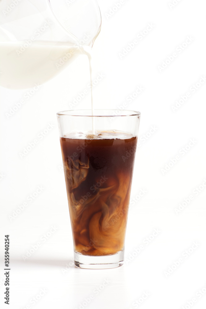 Milk is poured into a glass with coffee on a white background. Vertical orientation. Milk is poured into a glass with coffee on a white background. Vertical orientation.