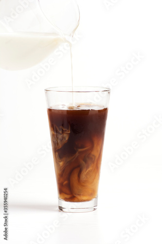 Milk is poured into a glass with coffee on a white background. Vertical orientation.
