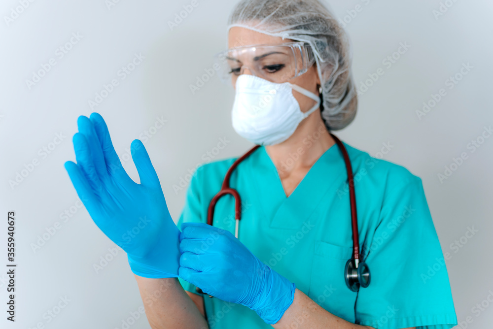 Female young nurse in a medical mask puts on protective surgical sterile gloves on her arm, isolated on gray background, protection against coronovirus. covid-19 protection Female young nurse in a medical mask puts on protective surgical sterile gloves on her arm, isolated on gray background, protection against coronovirus. covid-19 protection