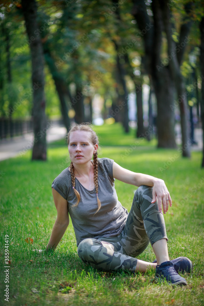 Beautiful woman is sitting on green grass. Woman in a dark brown t-shirt and khaki military pants. Young girl in the park. Beautiful woman is sitting on green grass. Woman in a dark brown t-shirt and khaki military pants. Young girl in the park.