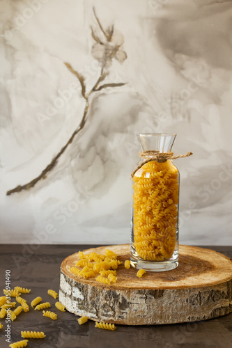 Spiral pasta in a glass jar on a wooden stand, scattered on the table