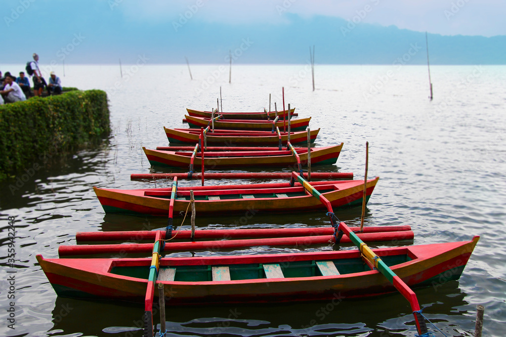 Colorful Wooden row boats with paddles at Batur lake under heavy clouds of thick fog