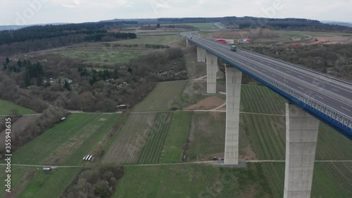 Hochmoselbrücke High Moselle Bridge in Rhineland-Palatinate Germany with traffic cars and trucks on a freeway highway cinematic panorama over fly aerial drone shot on a sunny cloudy day 30p photo