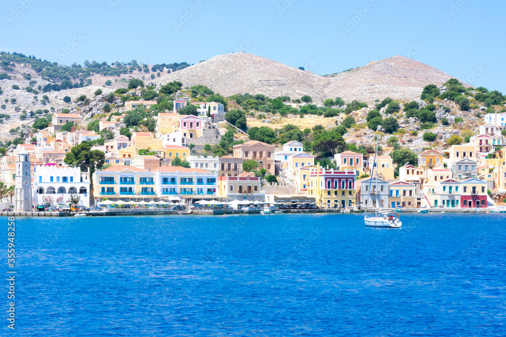 A lot of tiny colorful houses on the rocky shore of Mediterrenean sea on Simy greek island in sunny summer day, tourism on exotic islands