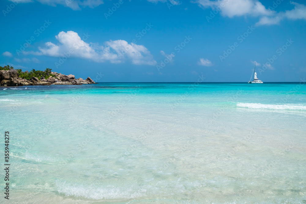 Ocean waves, white boat, pristine blue color lagoon and granite rocks on Anse Coco beach, La Digue Island, Seychelles