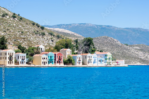 A lot of tiny colorful houses on the rocky shore of Mediterrenean sea on Simy greek island in sunny summer day, tourism on exotic islands