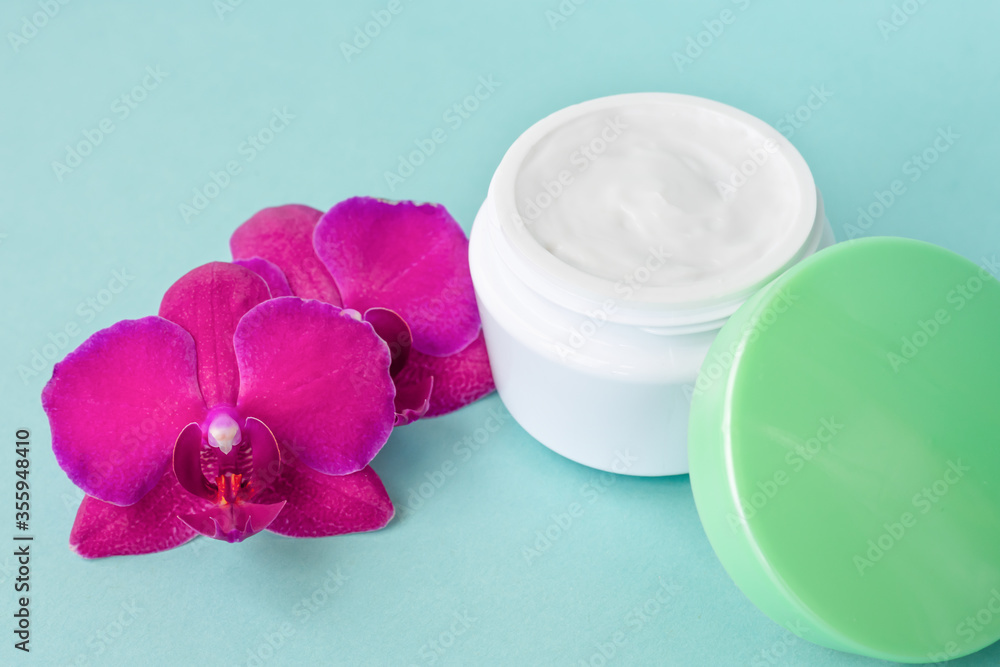 Cream in white jar with green cap on mint background with beautiful bright magenta orchid flowers. Soft cream with orchid extract for moisturizing skin. Eco cosmetic product Cream in white jar with green cap on mint background with beautiful bright magenta orchid flowers. Soft cream with orchid extract for moisturizing skin. Eco cosmetic product