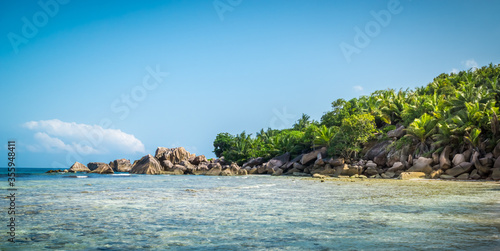 Panoramic view of nice tropical sandy beach with famous granite rocks on Anse Coco beach, La Digue Island, Seychelles. Holiday and vacation concept. Tropical beach on background blue sky