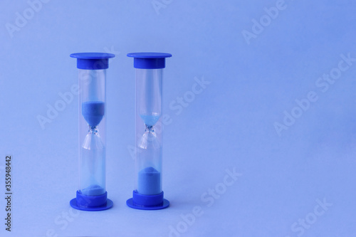 Two hourglass with falling sand inside of them as a symbol of running time, lifetime and no time. Sand watches with a big and little amount of blue sand as metaphor of rushing time.