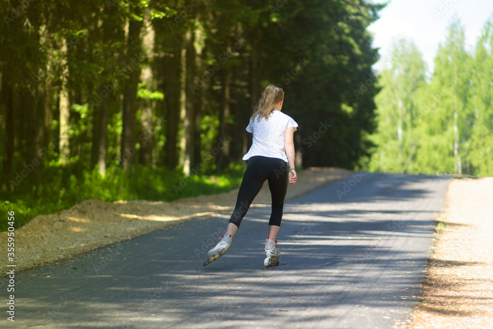 A girl rides roller skates on an asphalt road in the Park in the summer.