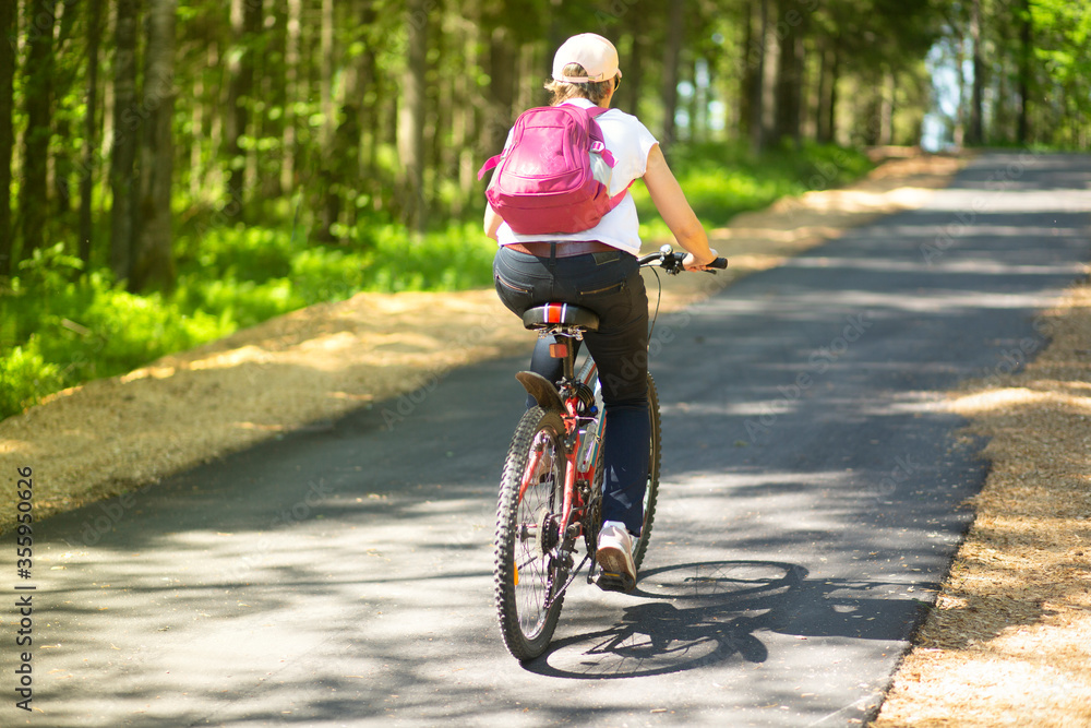 A woman rides a Bicycle on an asphalt road in the Park in the summer.